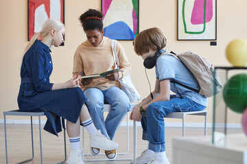 Group of three teenagers sitting in circle doing school project in modern art gallery or museum