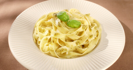 Pasta with pesto on a plate. Serving fettuccine with pesto on a brown background. Italian food with...