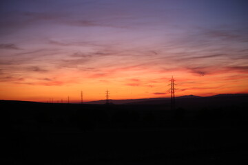 Silhouettes of high voltage lines running across vast land at red sunset