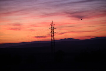 Silhouettes of high voltage lines running across vast land at red sunset