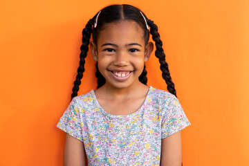 Portrait of happy biracial schoolgirl wearing t shirt over orange background at elementary school
