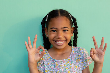 Biracial schoolgirl doing sign language gestures over blue background at elementary school