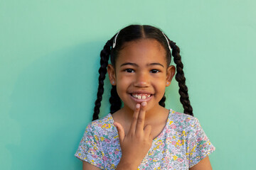 Biracial schoolgirl doing sign language gestures over blue background at elementary school