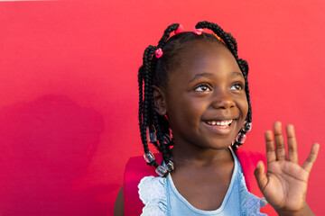 Happy african american schoolgirl waving hand over pink background at elementary school
