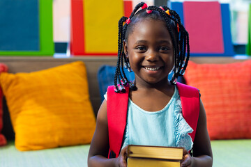 Portrait of happy african american schoolgirl with books in colourful room at elementary school