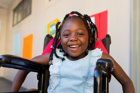Portrait of happy african american schoolgirl sitting in wheelchair at elementary school corridor