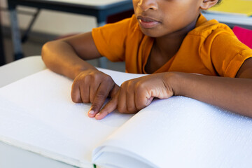 Focused biracial schoolboy reading braille with hands in classroom - Powered by Adobe