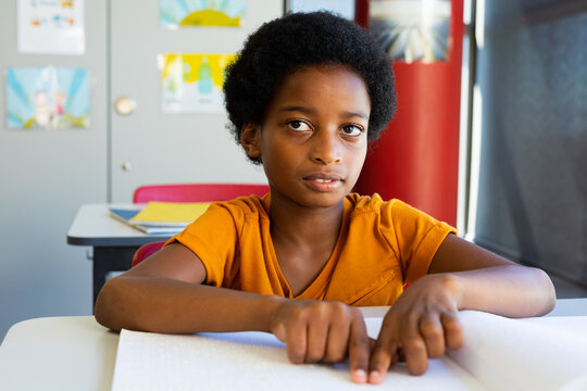 Focused biracial schoolboy reading braille with hands in classroom