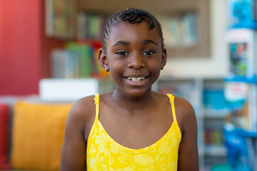 Portrait of happy african american schoolgirl wearing yellow dress in classroom