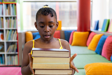 Shocked african american schoolgirl holding books over couch with colourful pillows