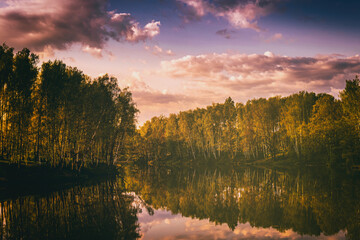 Sunrise or sunset on a lake or river with cloudy sky reflection in the water in summertime. Aesthetics of vintage film.