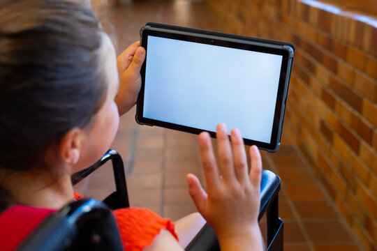 Caucasian schoolgirl sitting in wheelchair and using tablet with copy space at school corridor - Powered by Adobe