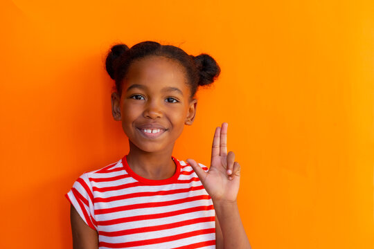 Happy african american schoolgirl doing oing sign language with hand over orange background