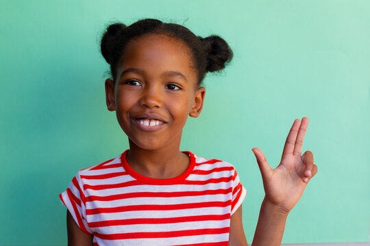 African american schoolgirl oing sign language with hand over blue background at elementary school