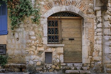 Fototapeta na wymiar Old wooden door of a traditional stone house on a street in the medieval town of Saint Paul de Vence, French Riviera, South of France