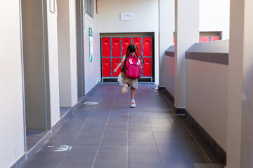 Biracial schoolgirl running with red school bag in corridor at elementary school