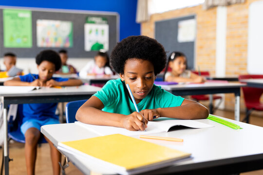 Portrait of happy african american elementary schoolboy writing in notebook at desk in class
