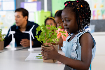 Happy african american girl with plant in ecology class at elementary school