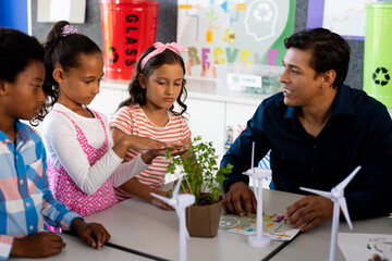 Happy diverse male teacher and children with ecology items in class at elementary school