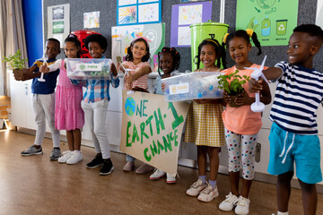 Portrait of happy diverse children with ecology items and plants in class at elementary school