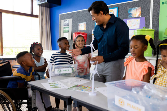 Happy diverse male teacher and children with ecology items in class at elementary school