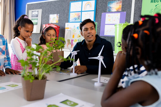 Happy diverse male teacher and children with windmills and plants in class at elementary school - Powered by Adobe