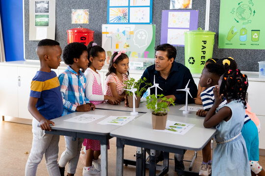 Happy diverse male teacher and children with ecology items in class at elementary school