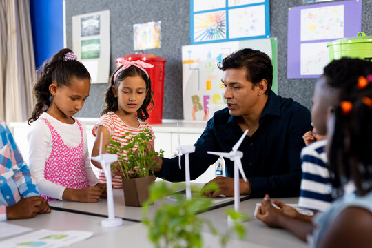 Happy diverse male teacher and children with ecology items in class at elementary school