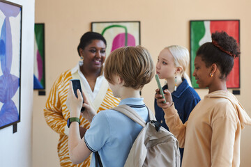 Diverse group of teenagers taking photos of abstract art in modern art gallery or museum