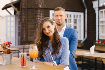 Portrait of a stylish young couple in love in blue flowers in summer in the city at a bar table, drinking cocktails