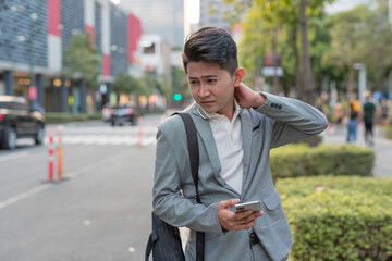 A young asian man suffers from a stiff neck from work while walking to a bus stop. Urban city...