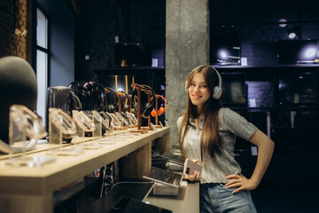Fototapeta na wymiar Close up of cute stylish happy girl testing and choosing headphones in a tech store