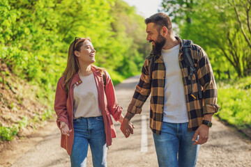 Happy couple hiking in nature on sunny day. Couple holding hands and walking on road.