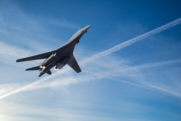 A modern military fighter plane flying with smoke and flames on blue sky with white airjet trails and copy space