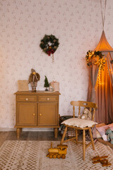 Interior of a children's room decorated for Christmas. A tent with toys and pillows, a Christmas tree, a wardrobe and a chair in beige tones
