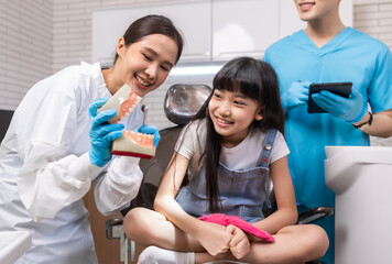 Fototapeta premium Female asain dentist holding tooth model and talking to child in dental clinic.