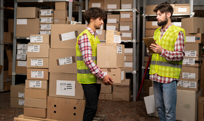Warehouse manager using digital tablet doing inventory and courier with boxes preparing goods for...