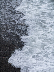 The violent foam from the waves on the black pebble beach 