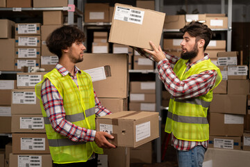 Two mixed race warehouse workers while recording inventory. Logistics employees working in warehouse in a large distribution center holding big boxes.