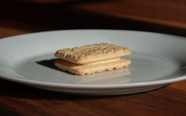 A solitary custard cream biscuit on a white plate. 