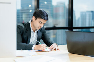 Handsome young businessman taking notes on paper at office The background is a blurred city.