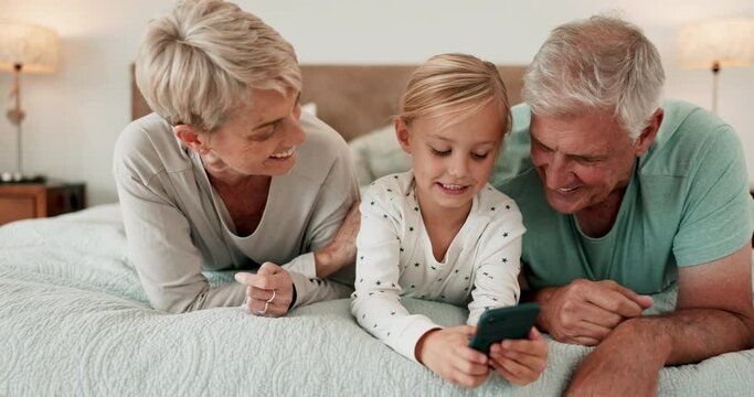 Phone, games and grandparents kissing a girl on a bed in the home for playing together or bonding. Love, kids or family with senior man and woman loving their granddaughter on a mobile in the bedroom