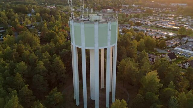 Aerial view of a water tower and residential area in backlight sunset. Orbit drone shot.