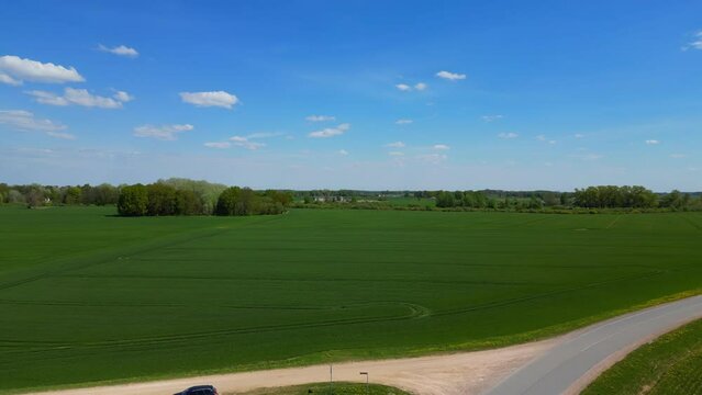 A black car parked next to a farm with nearly endless green fields of young crops