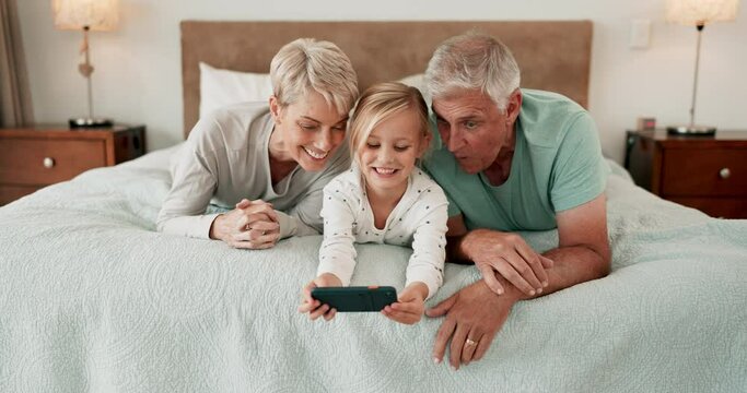 Phone, games and a girl with her grandparents on a bed in the home for playing together or bonding. Love, kids or family with senior man and woman with their granddaughter on a mobile in the bedroom
