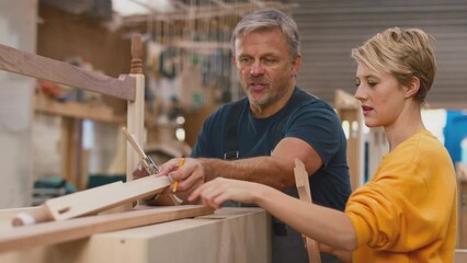 Mature male carpenter sharing woodworking skills with female apprentice in furniture factory - shot in slow motion