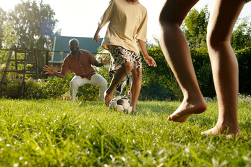 Barefoot children and their father playing footbal on green lawn together and having fun on summer...