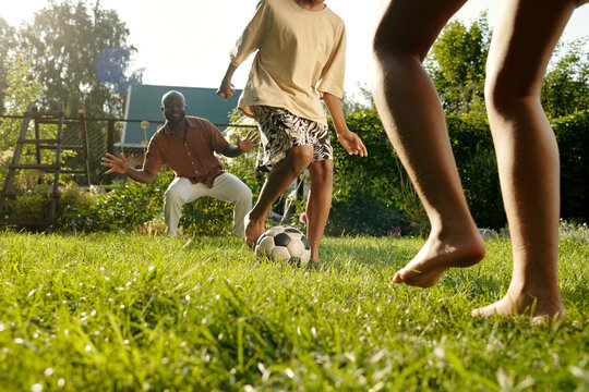 Barefoot children and their father playing footbal on green lawn together and having fun on summer day on the countryside during vacation