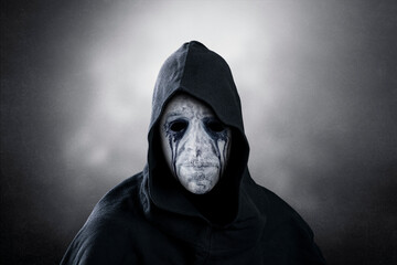 Spooky figure with hooded cape over dark misty background