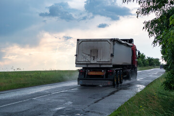 Heavy truck vehicle driving wet rural asphalt road driveway in stormy rainy weather with epic...